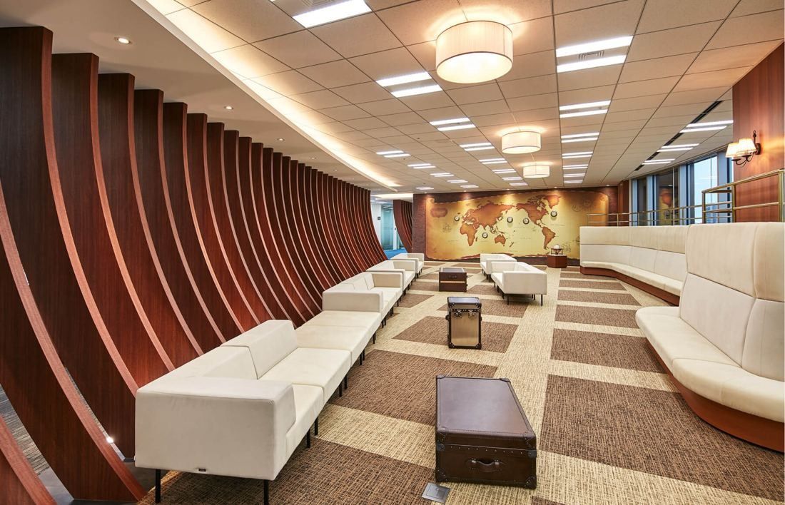 SEGA: Long waiting area with white sofas framed by curved wooden ribs and a world map at the end