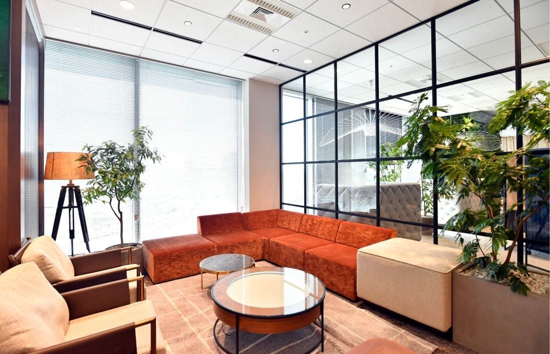 SEGA: Lounge with an orange sofa, round glass table and plants by a steel-framed window
