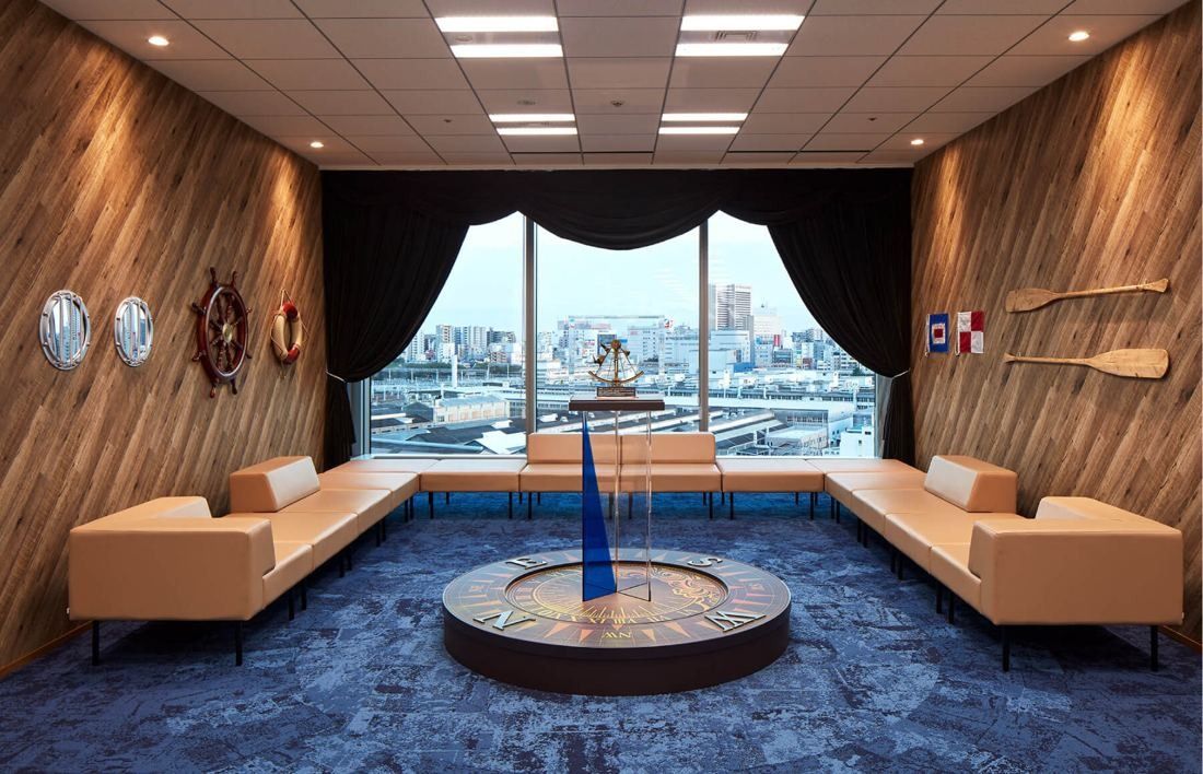SEGA: Lounge with wood-paneled walls, portholes, a ship's wheel, curtains and a compass table facing a window