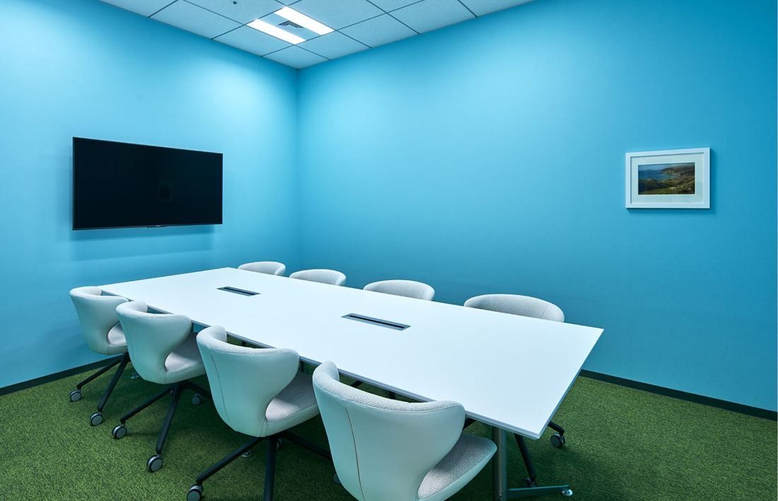 SEGA: Meeting room with bright blue walls, green floor, a white table and a wall screen