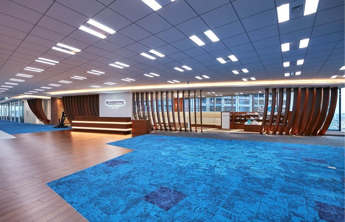 SEGA: Wide reception floor with blue carpet, wooden curved ribs and a long reception counter