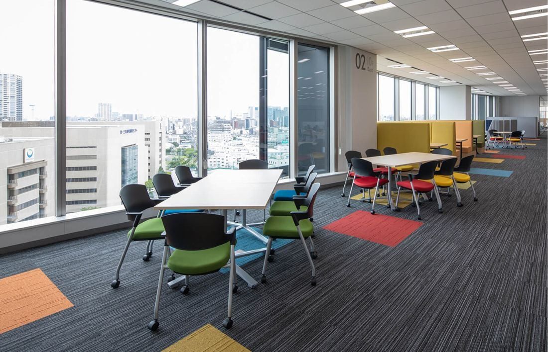 SEGA: Window-side meeting tables with colorful chairs and carpet patches