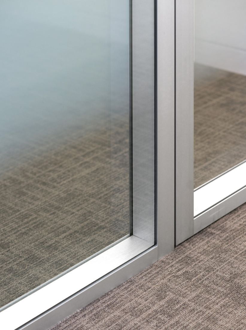 Shell: Close-up of a frosted glass partition with slim metal frames on patterned grey carpet