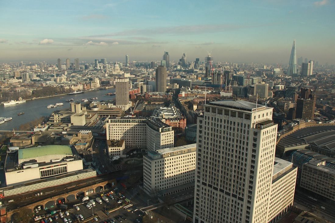 Shell: High aerial view over the tower and surrounding low buildings towards the City of London skyline