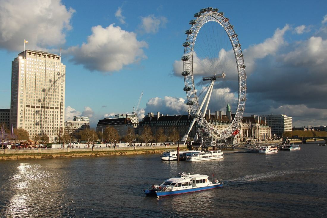 Shell: Stone tower beside a giant observation wheel and a long riverside building, with boats on the Thames