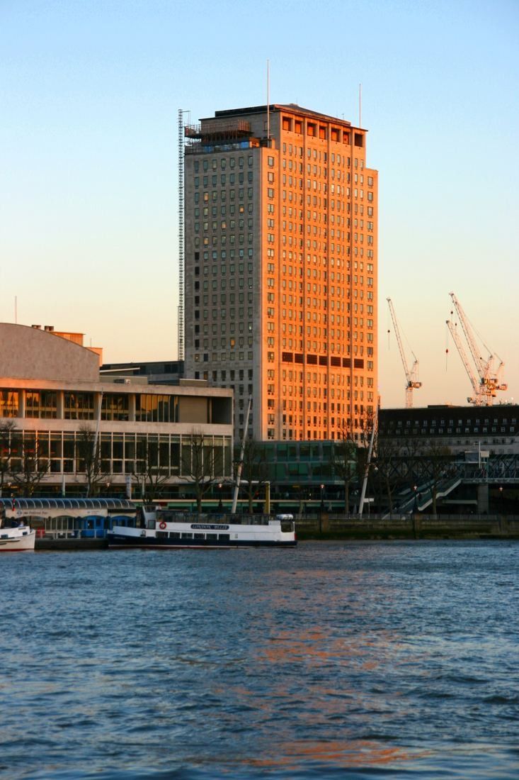Shell: Tower lit orange by the setting sun above the river Thames and the riverside walk