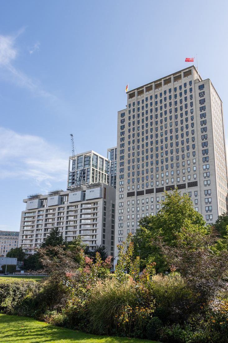 Shell: Tower rising behind planted gardens and newer residential blocks under a blue sky