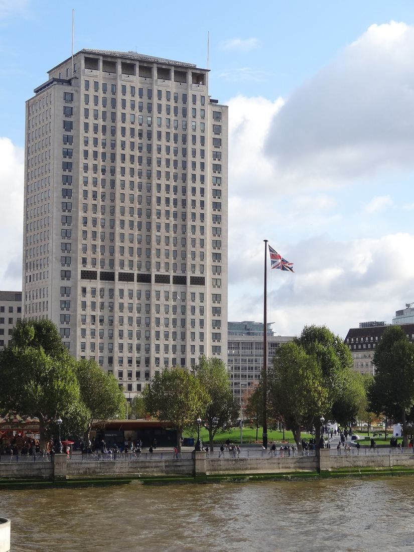 Shell: Tower with a flag on a pole in front, seen over the river wall and trees