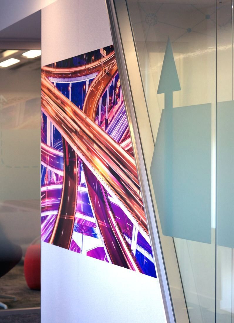Shell: Wall graphic of glowing road interchanges beside a frosted glass wall with an arrow motif