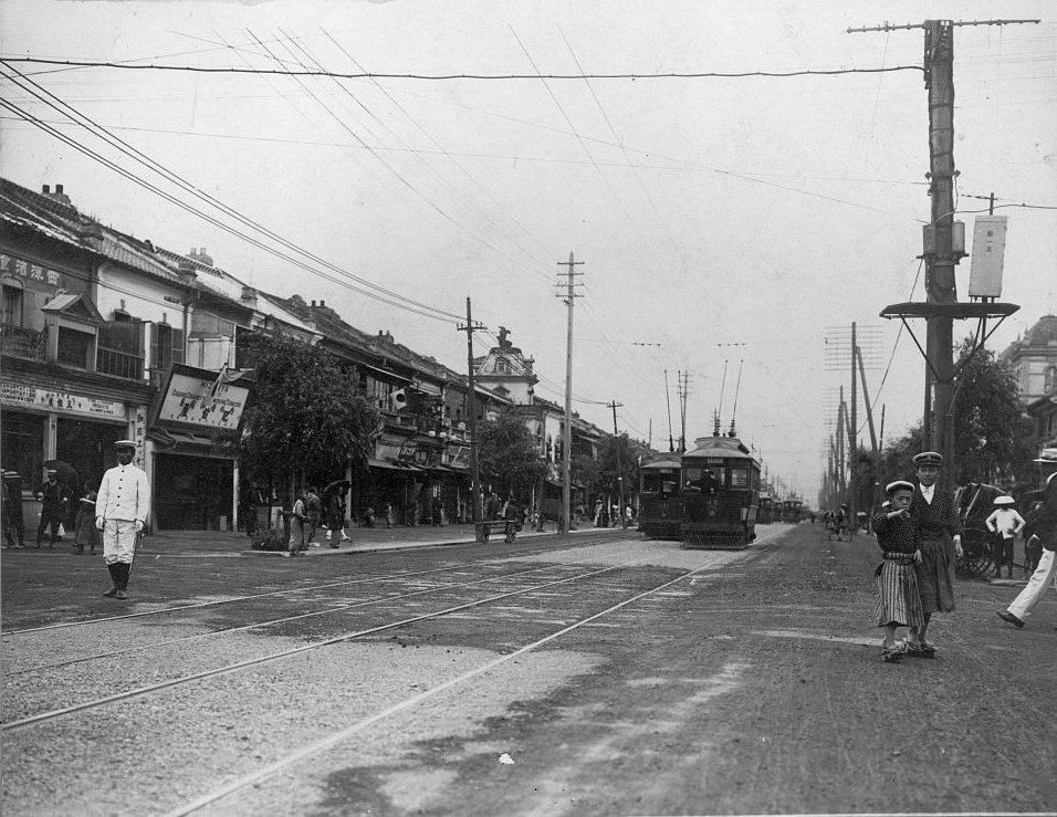 Old photograph of a Tokyo street with low shops, poles and a tram in the distance