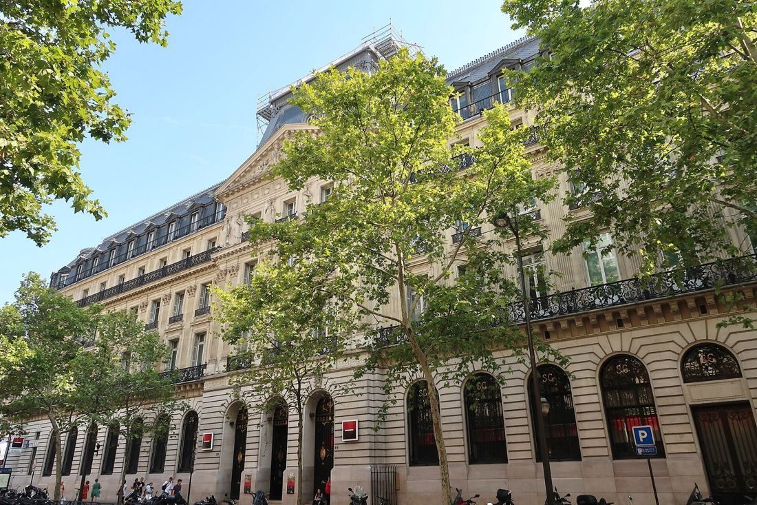 Société Générale: Arched ground-floor windows and stone facade seen through leafy trees