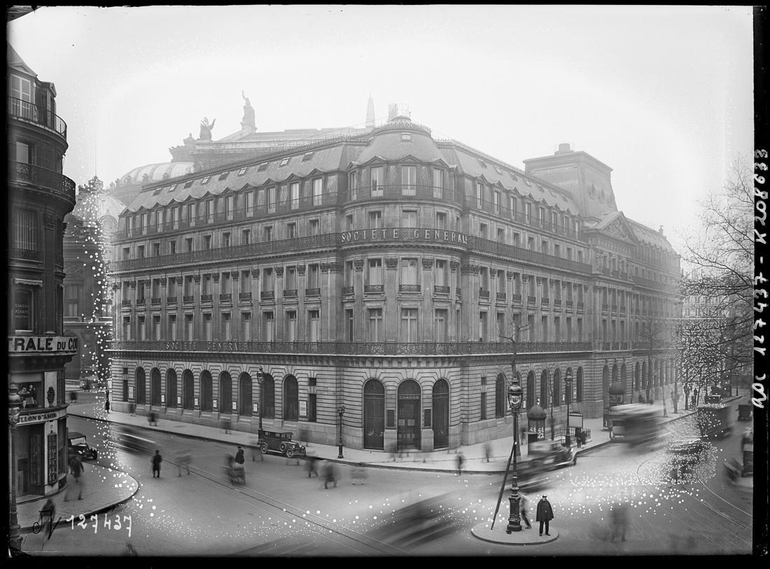 Black-and-white photo of the large domed corner building lettered Société Générale, with old cars and passers-by