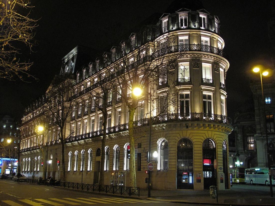 Société Générale: Corner of a lit-up stone building with a domed rotunda at night, street lamps in front