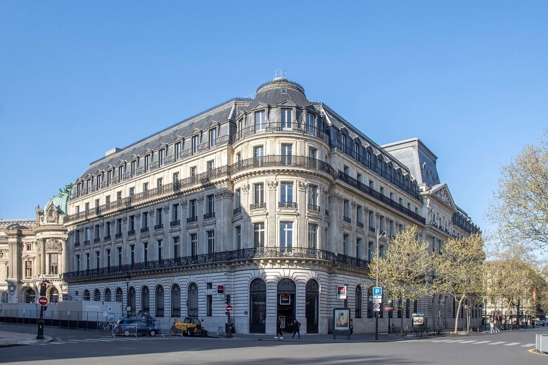 Société Générale: Long Belle Époque stone building with a domed corner and mansard roof on a sunny Paris boulevard