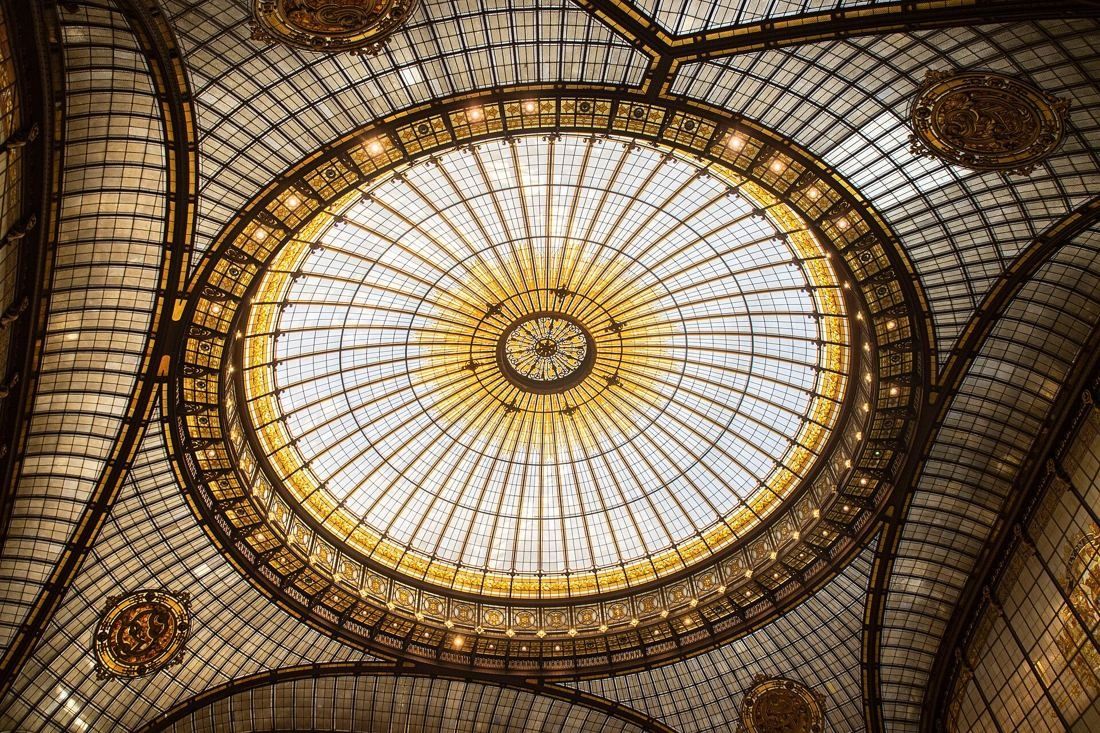 Looking up into a large round stained-glass dome in amber and gold, framed by ornate ironwork