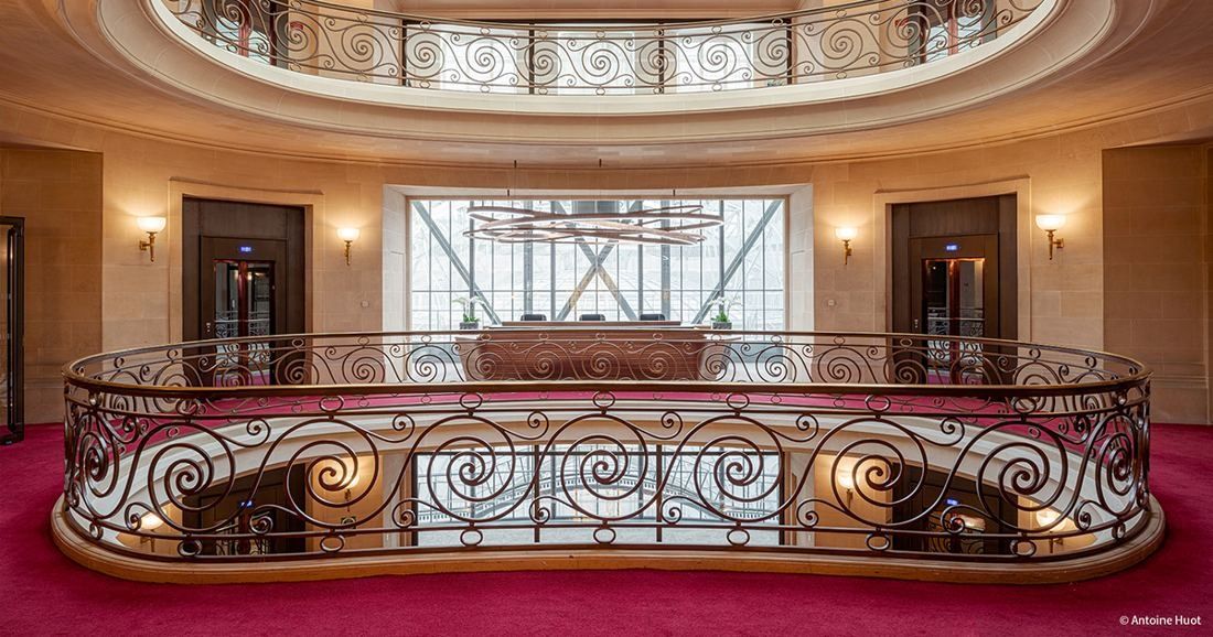 Société Générale: Round opening with a curving wrought-iron balustrade on a red carpeted landing, wall lamps around