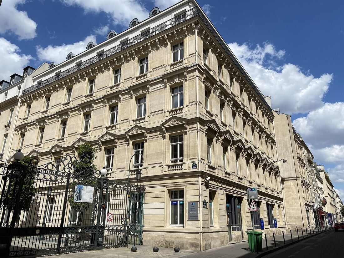 Stone corner building with iron gates on a narrow Paris street under a blue sky