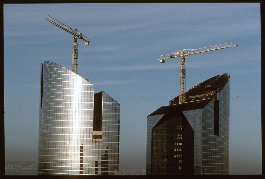 Two glass towers under construction with tower cranes on top