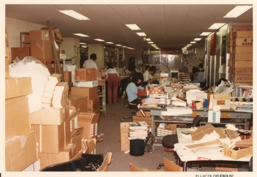 Crowded office with stacks of cardboard boxes, desks and fluorescent ceiling lights