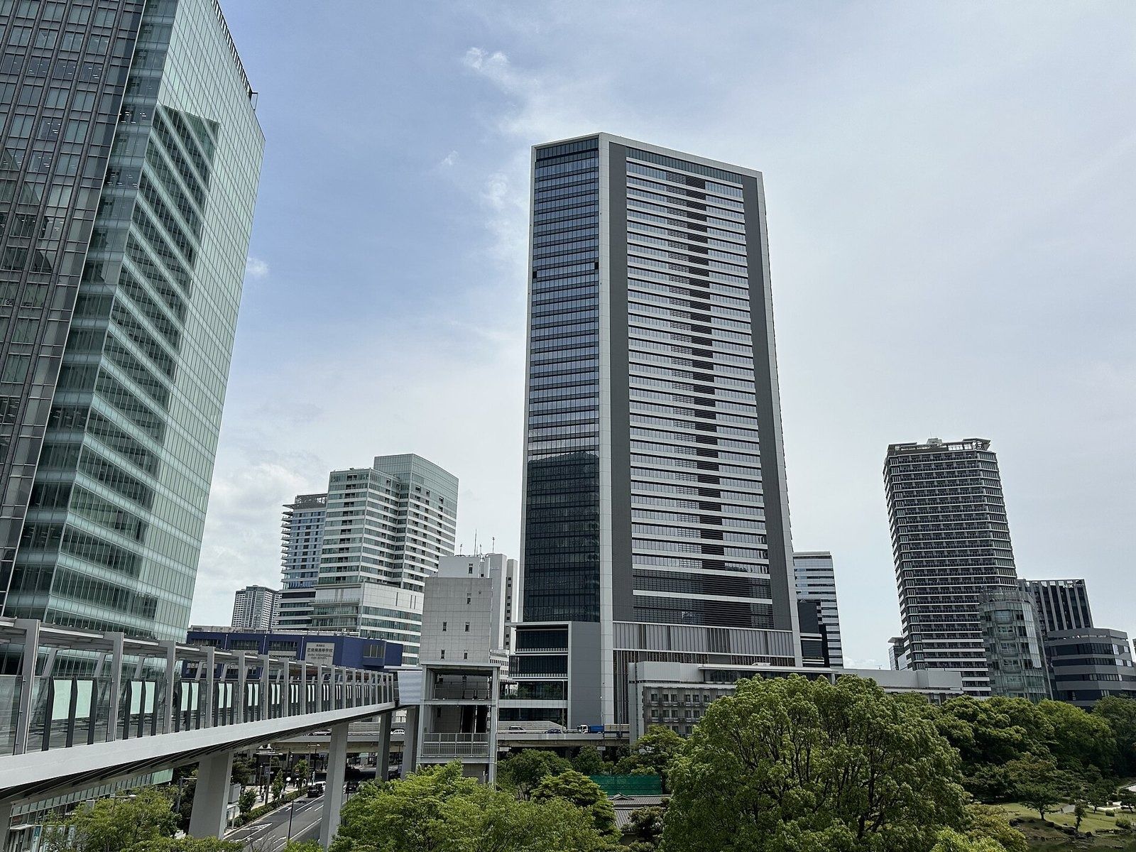 Tall glass office tower above trees and an elevated walkway