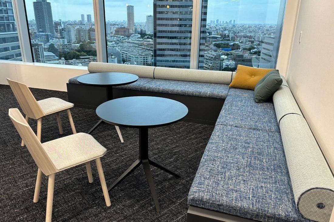 Square Enix: Corner seating with a sofa and round tables by windows over the city