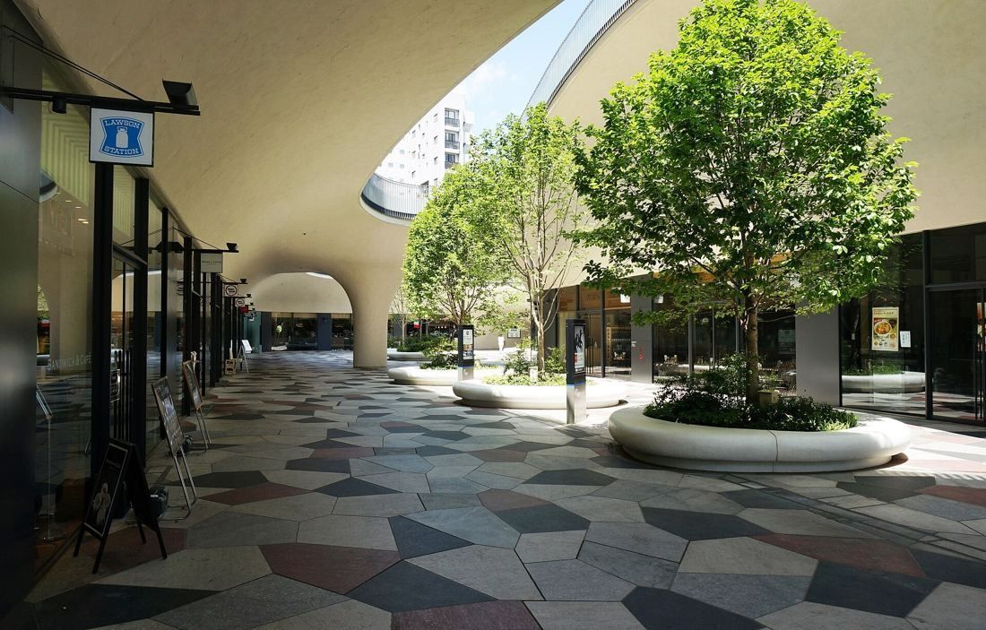 Square Enix: Curved covered walkway around a paved courtyard with trees in round planters