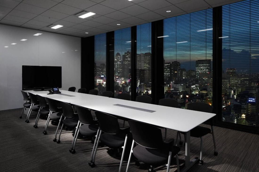 Square Enix: Long white meeting table with black chairs and a wall of windows at night
