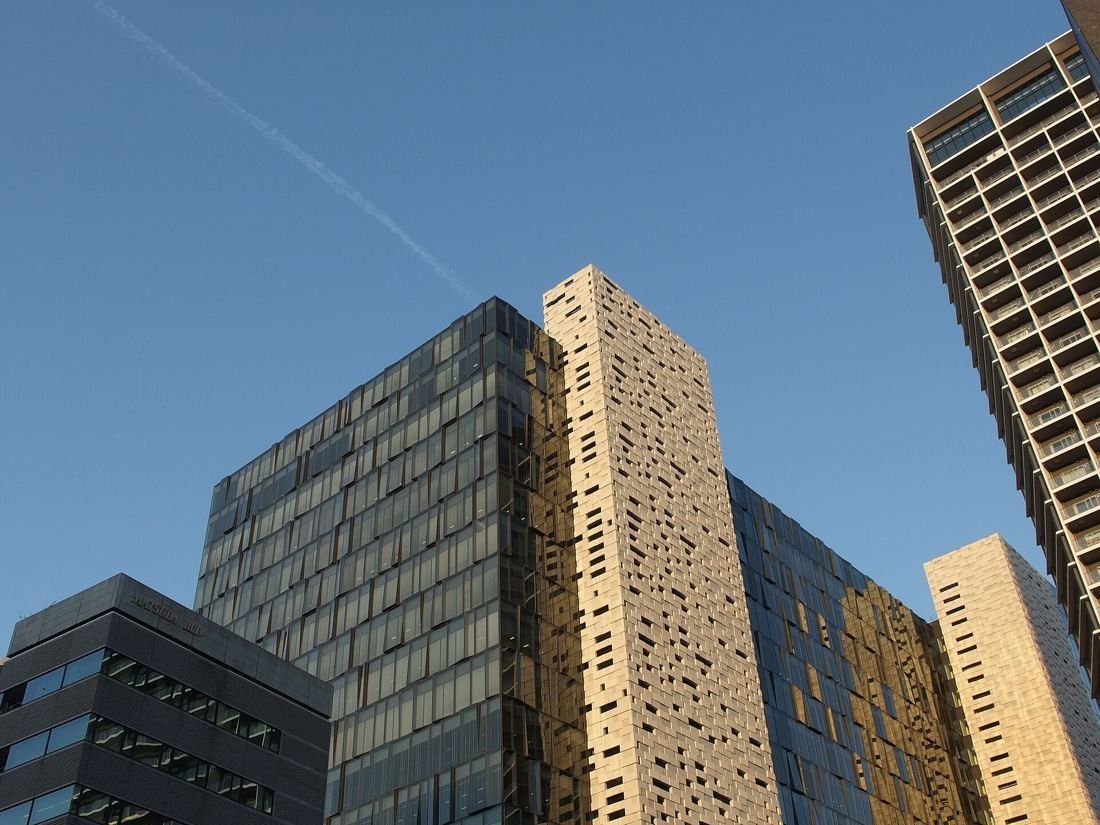 Office tower with a perforated beige facade and dark glass wings against a blue sky