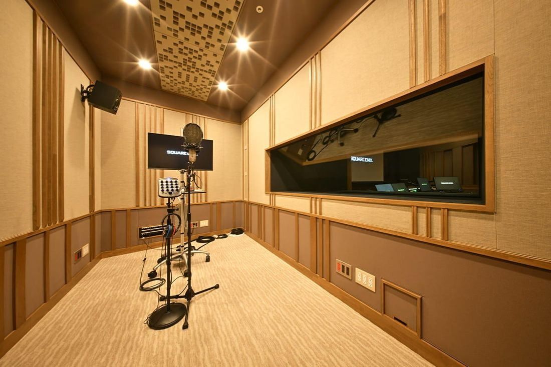 Square Enix: Recording booth with a microphone stand, wooden walls and a control-room window