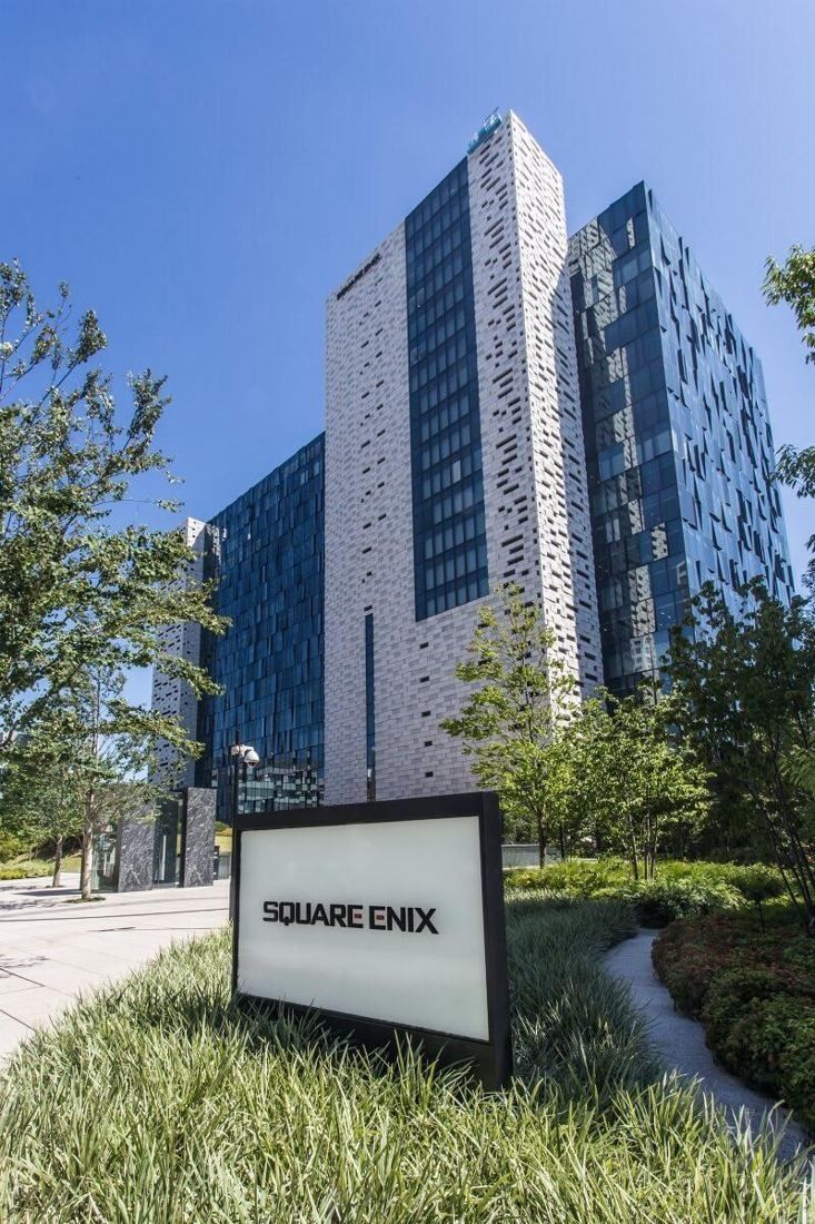 Square Enix: Tall office building with a patterned facade behind a garden and a low sign