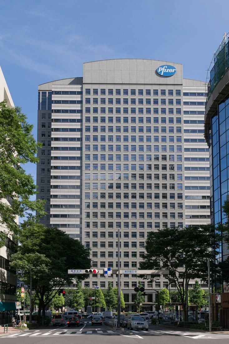 Tall pale office tower seen from the street between trees