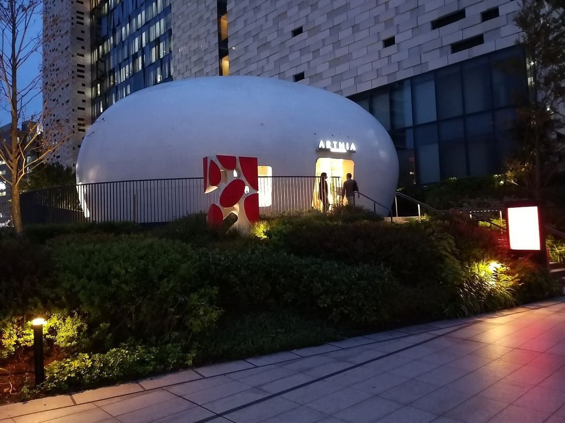 Square Enix: White rounded pavilion lit at dusk among garden planting