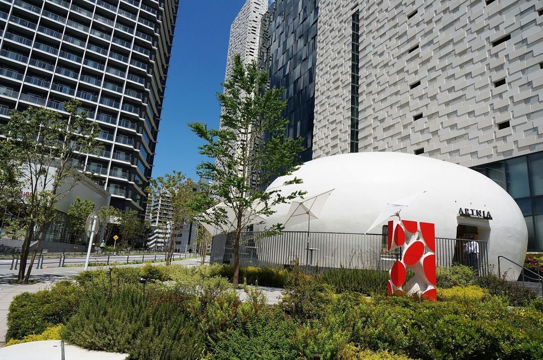 Square Enix: White rounded pavilion with a red sculpture, set in planting below office towers
