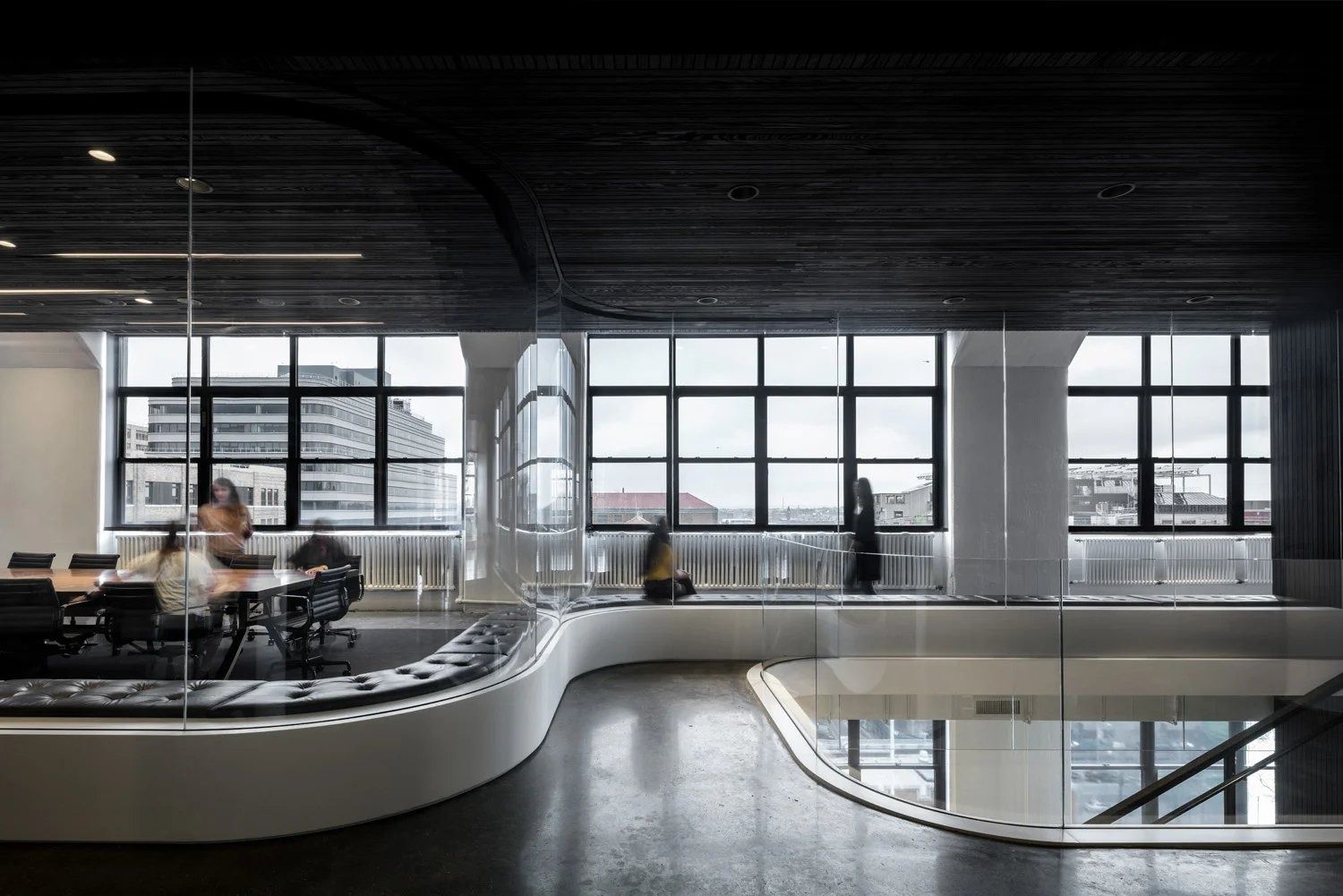 Squarespace: Curved floor opening with a white edge and glass rail, desks and tall windows behind
