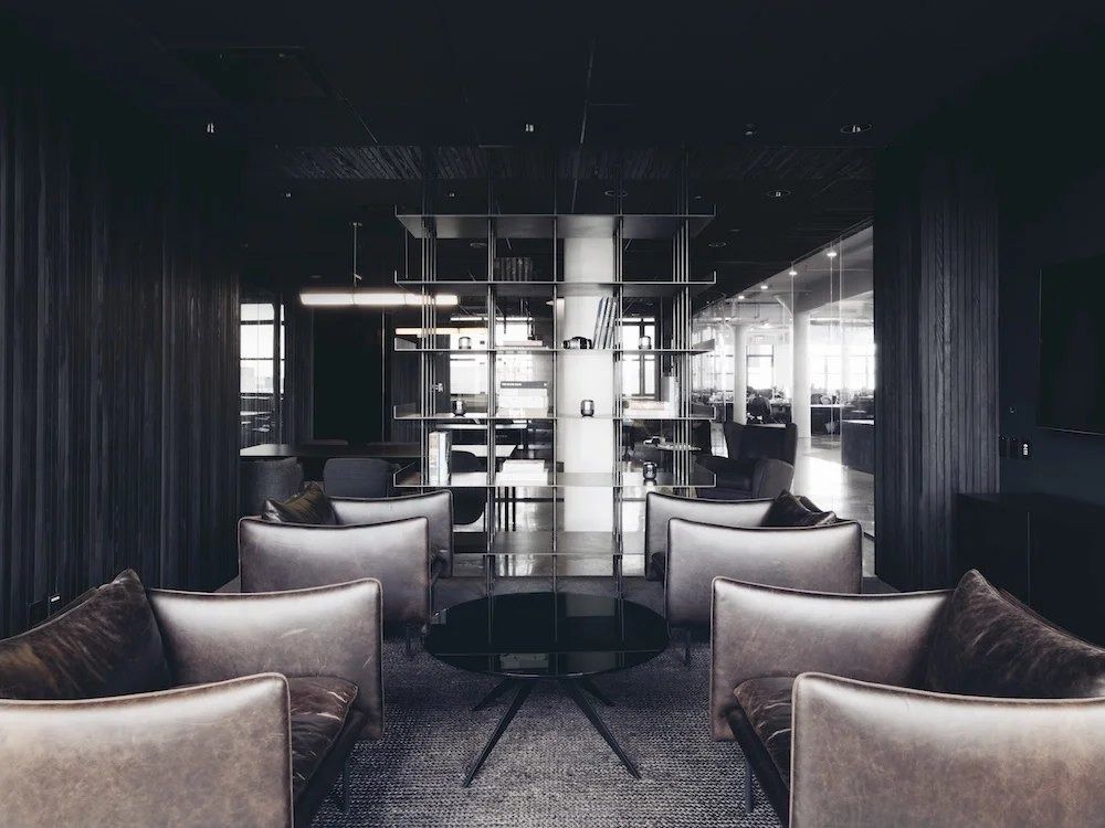 Squarespace: Dark lounge with leather armchairs around a round table, framed by black panels and shelving