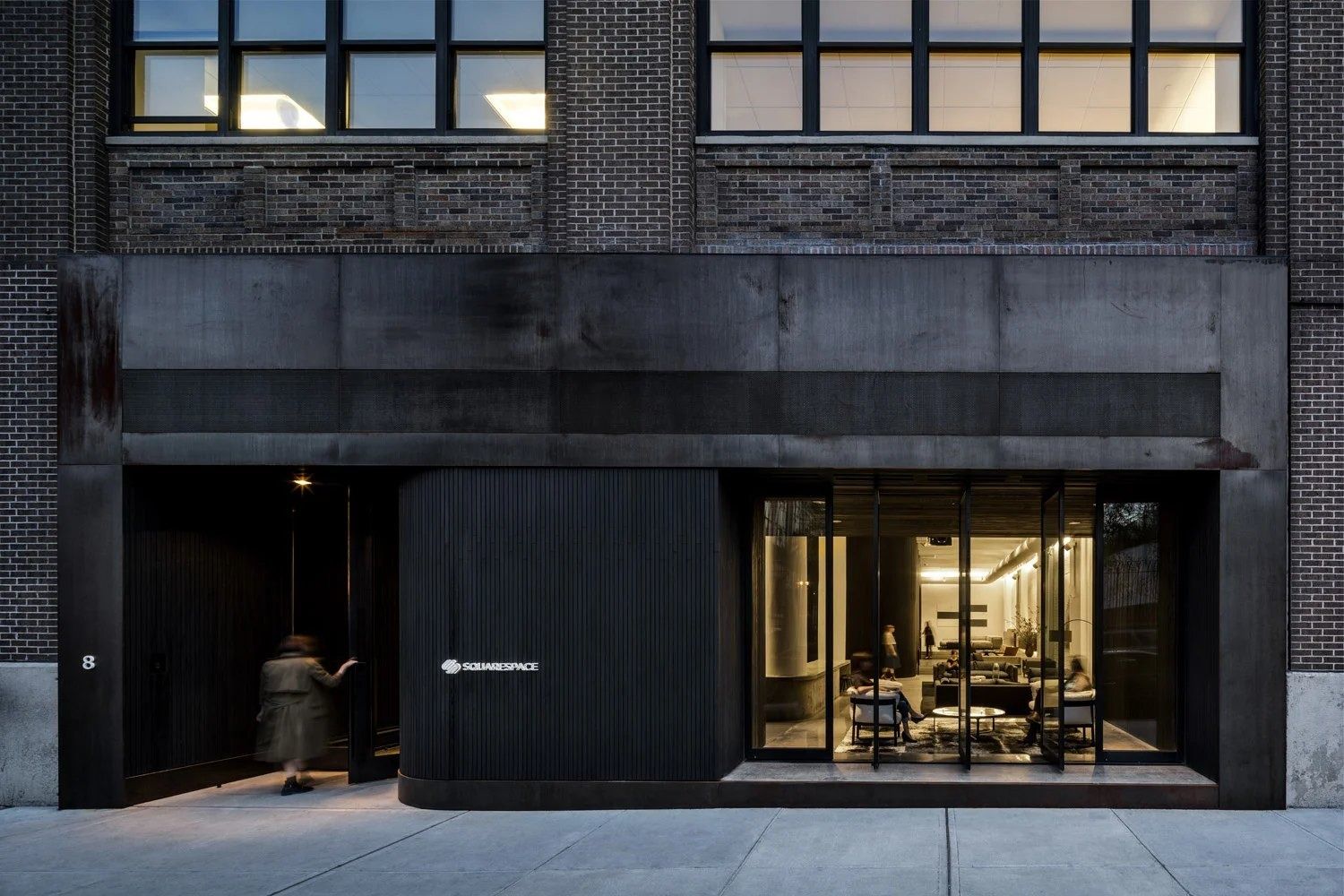 Squarespace: Dark metal-clad ground-floor entrance set into a brick and stone loft building, lit at dusk
