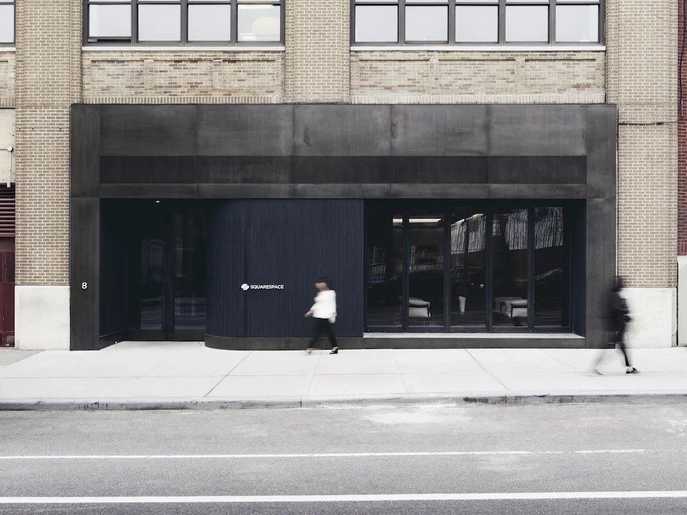 Squarespace: Daytime view of the dark metal entrance at the base of a stone and brick building, seen from across the street