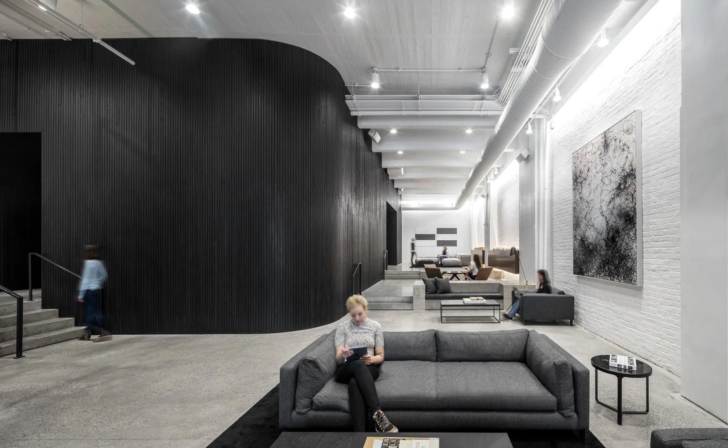 Squarespace: Long lounge with grey sofas, a curved black wood-slatted wall and white brick hung with a large artwork