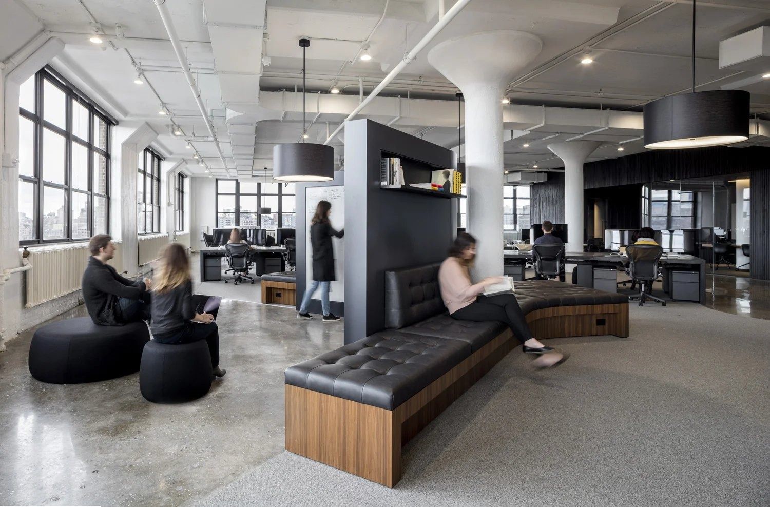 Squarespace: Office floor with black tufted leather bench seating, round pendants, white columns and desks by large windows