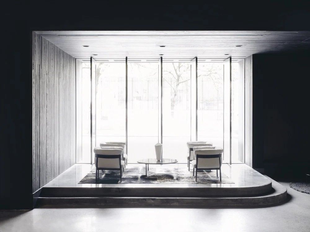 Squarespace: Raised seating area with armchairs inside a dark wood frame, in front of tall windows