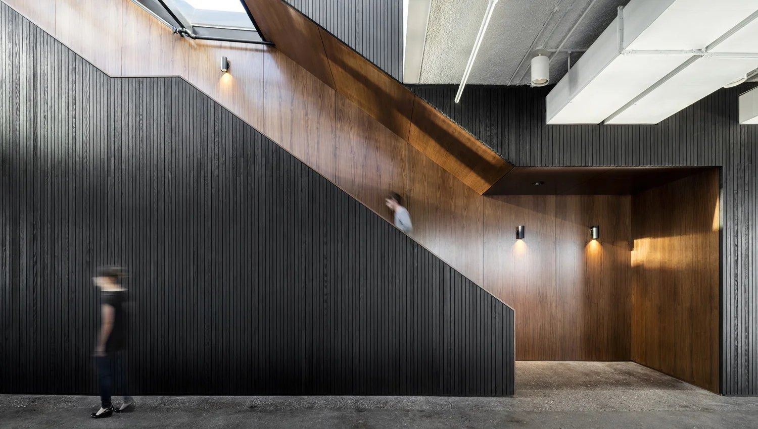 Squarespace: Staircase wrapped in dark vertical wood panels rising beside a white ceiling