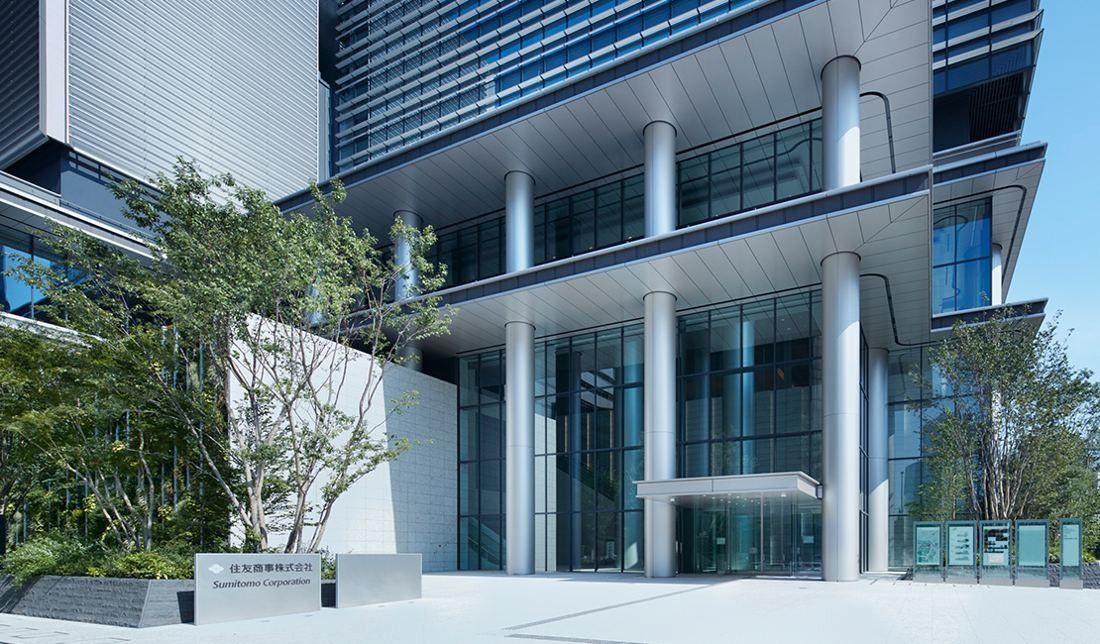 Glass entrance of a tall office tower with slim columns and trees in front
