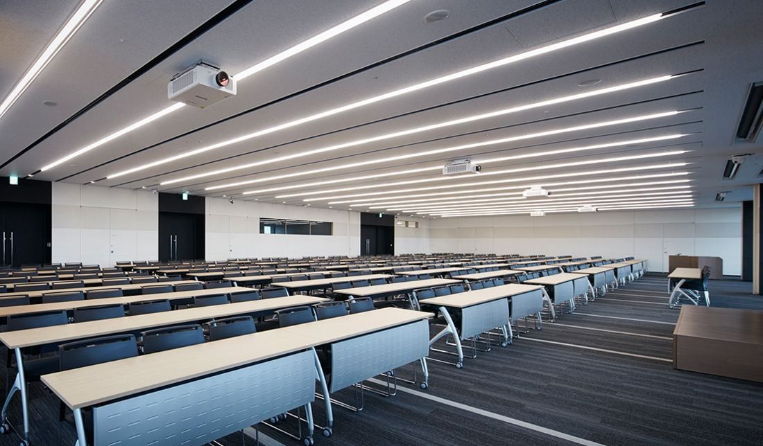 Sumitomo Corporation: Large hall with rows of seminar tables under linear ceiling lights