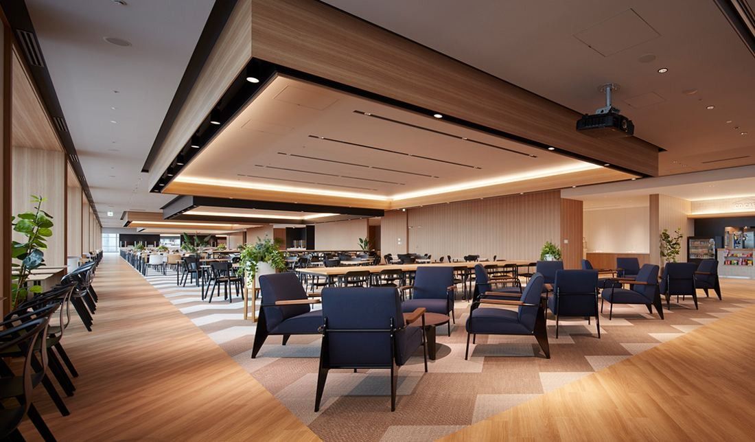Sumitomo Corporation: Long open lounge with wood floors, dark armchairs and plants beside tall windows