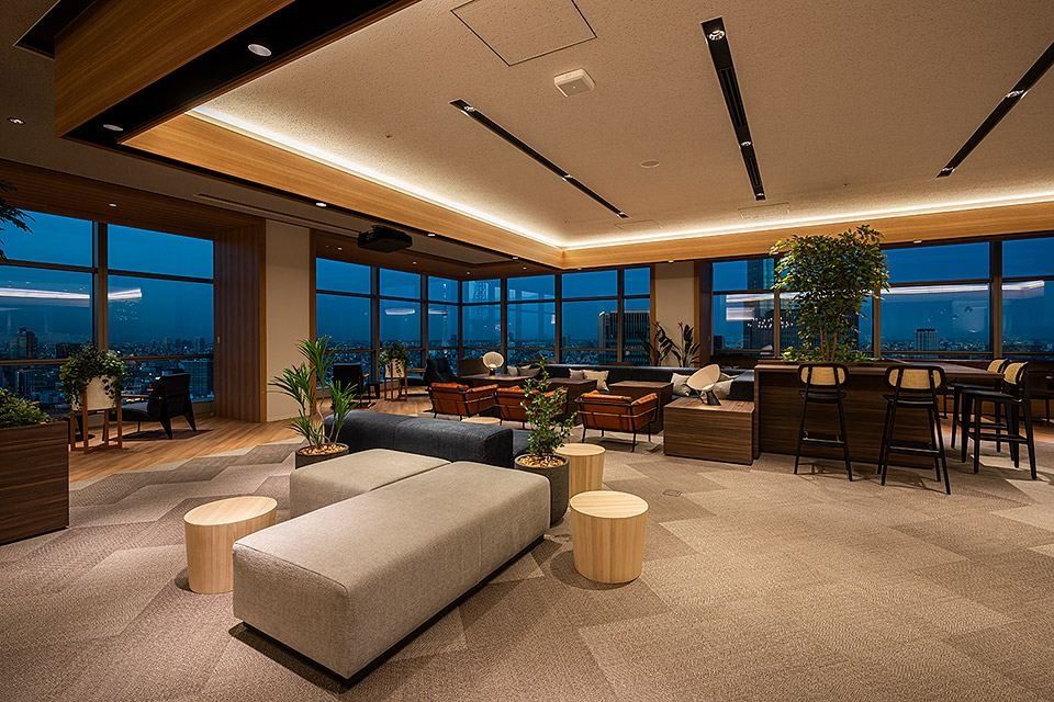 Sumitomo Corporation: Lounge with low sofas, stools and bar seating beside windows overlooking the city at dusk