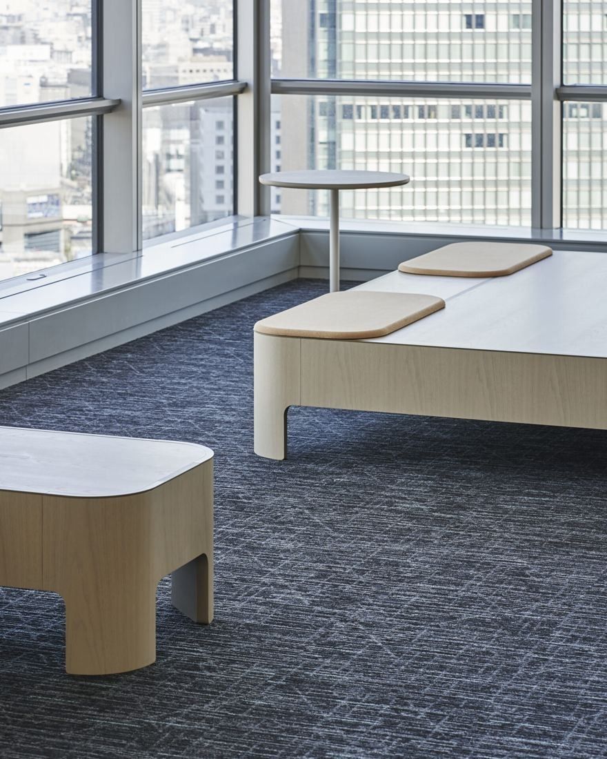Sumitomo Corporation: Low wooden benches with cushions on blue carpet beside a window