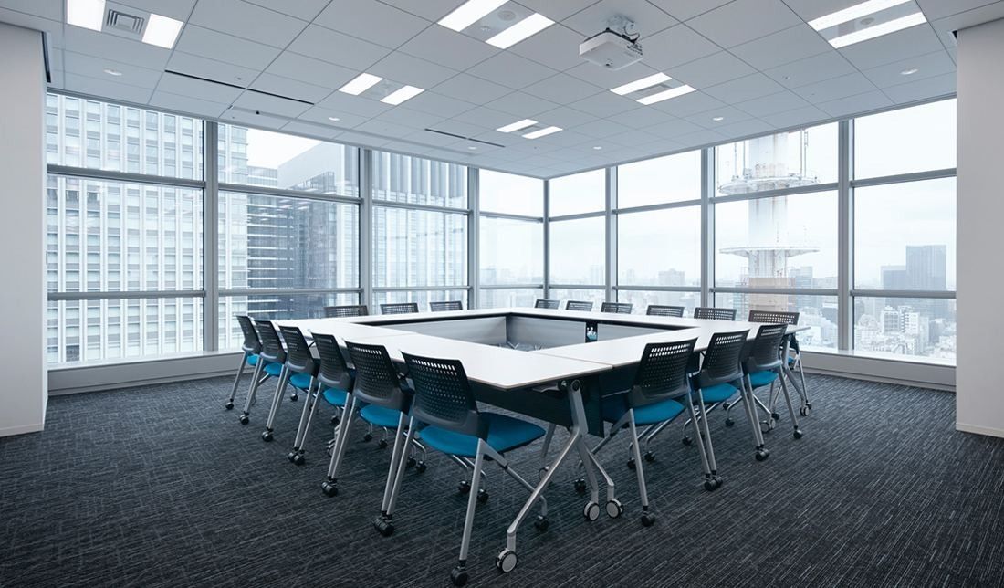 Sumitomo Corporation: Meeting room with tables in a square and teal chairs, city towers outside