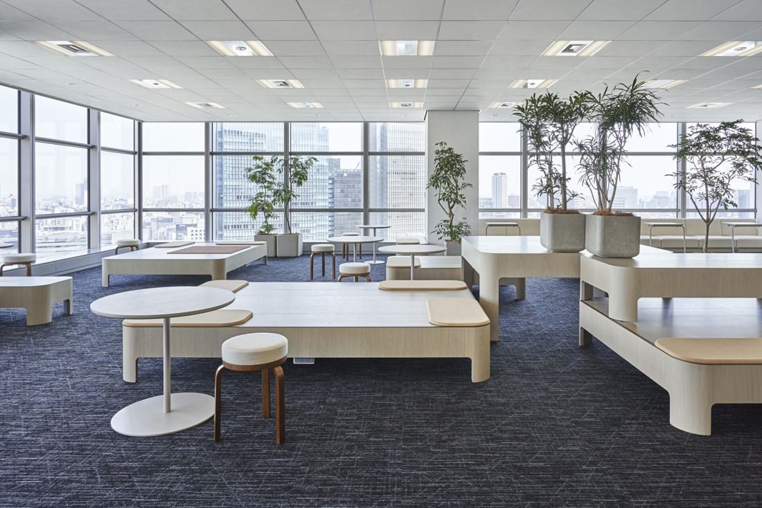 Sumitomo Corporation: Open floor with light wooden platforms, round tables, stools and potted trees by the windows