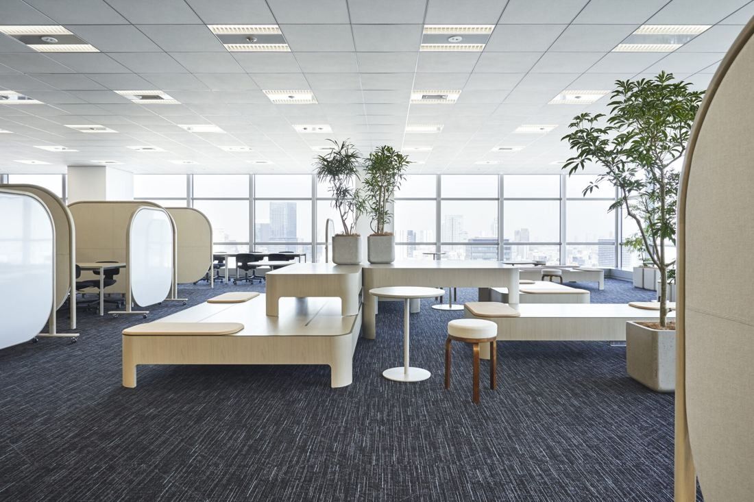 Sumitomo Corporation: Open office area with light wooden benches, round tables, curved booths and potted trees