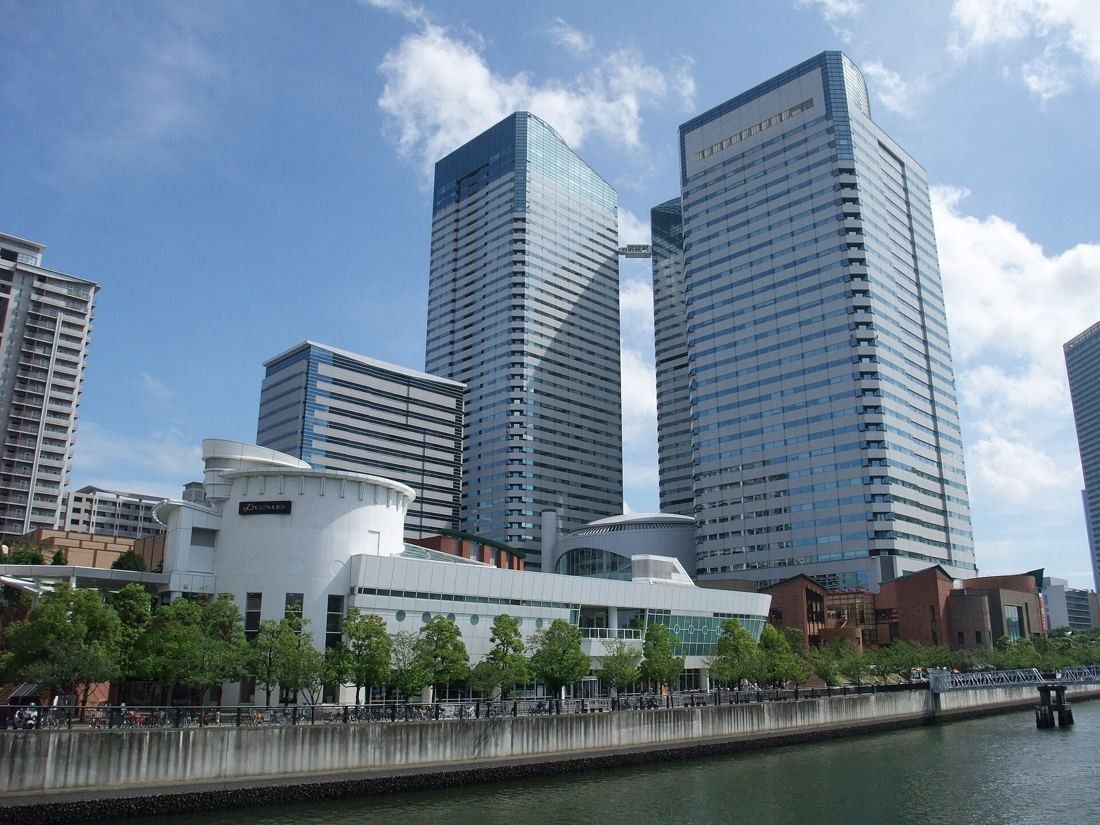 Twin glass office towers and a low curved building seen across a canal